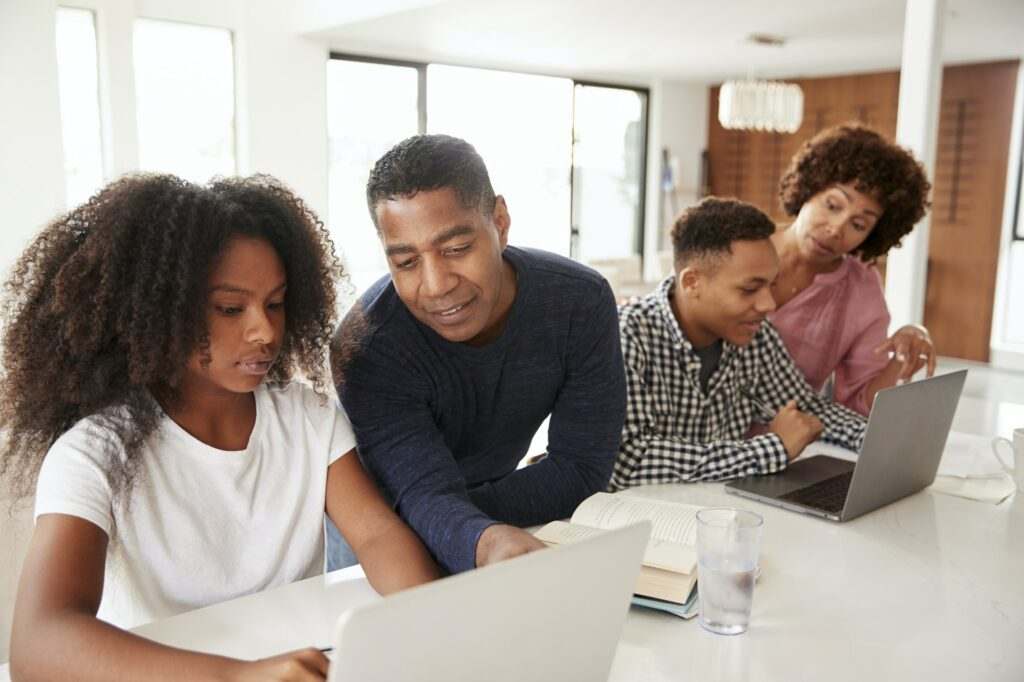 Middle aged black parents helping their teenage kids using laptops to do homework, close up